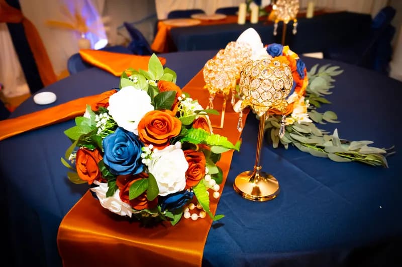 Navy table with an orange satin runner, rose arrangement and gold crystal candle holders