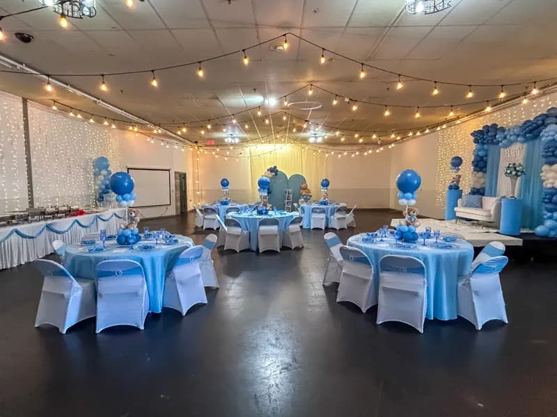 Baby shower hall with light blue linens, string lights and teddy bear centerpieces
