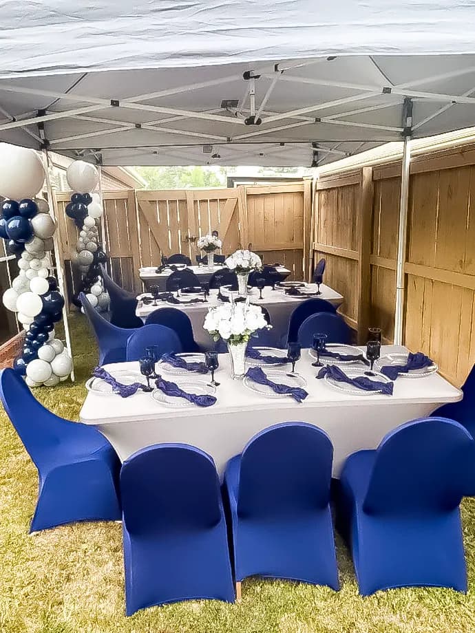 Backyard tent dinner with navy chair covers, white linens and navy and white balloon columns