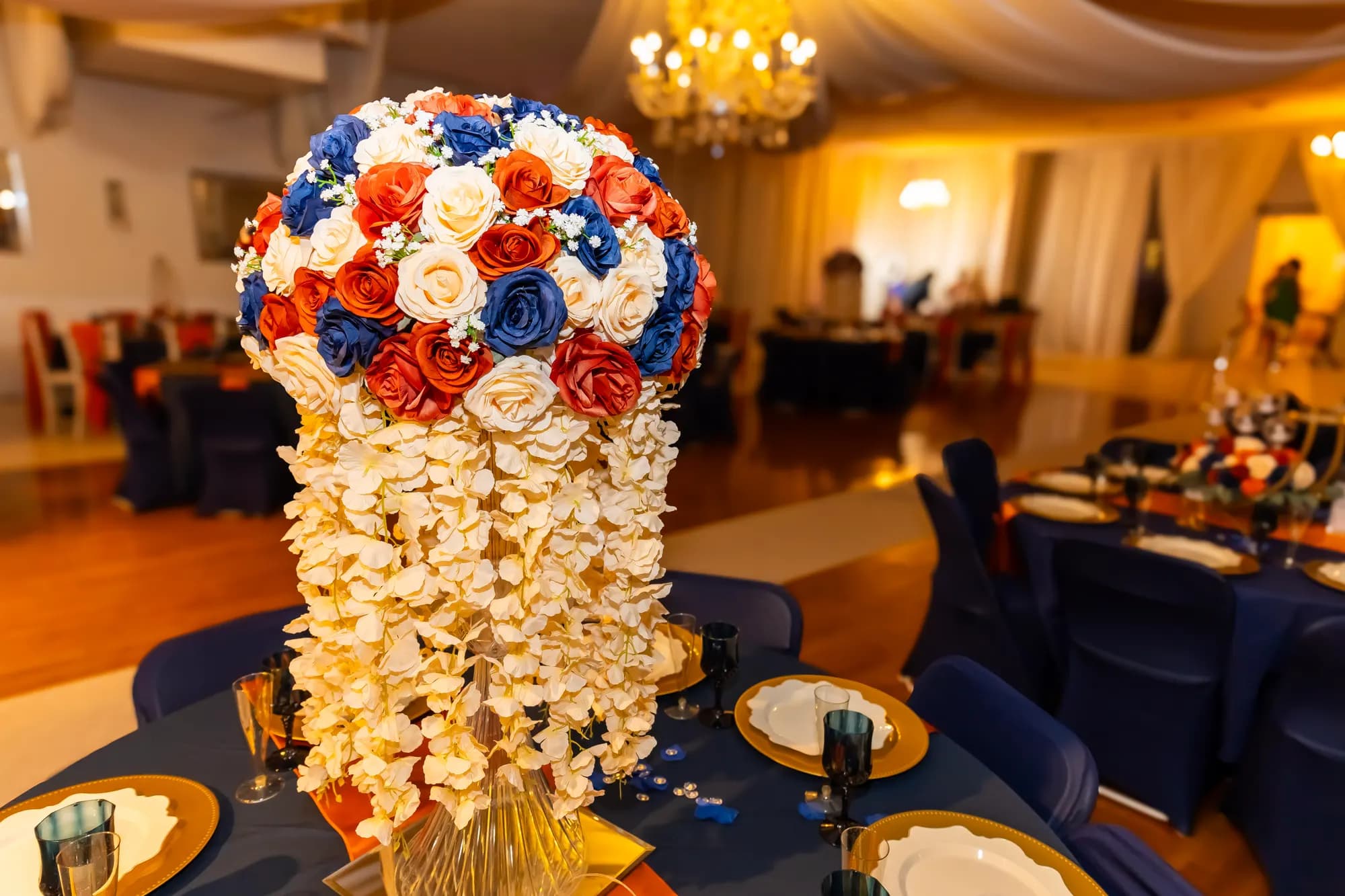 Cascading centerpiece of navy, orange and ivory roses with hanging white blooms