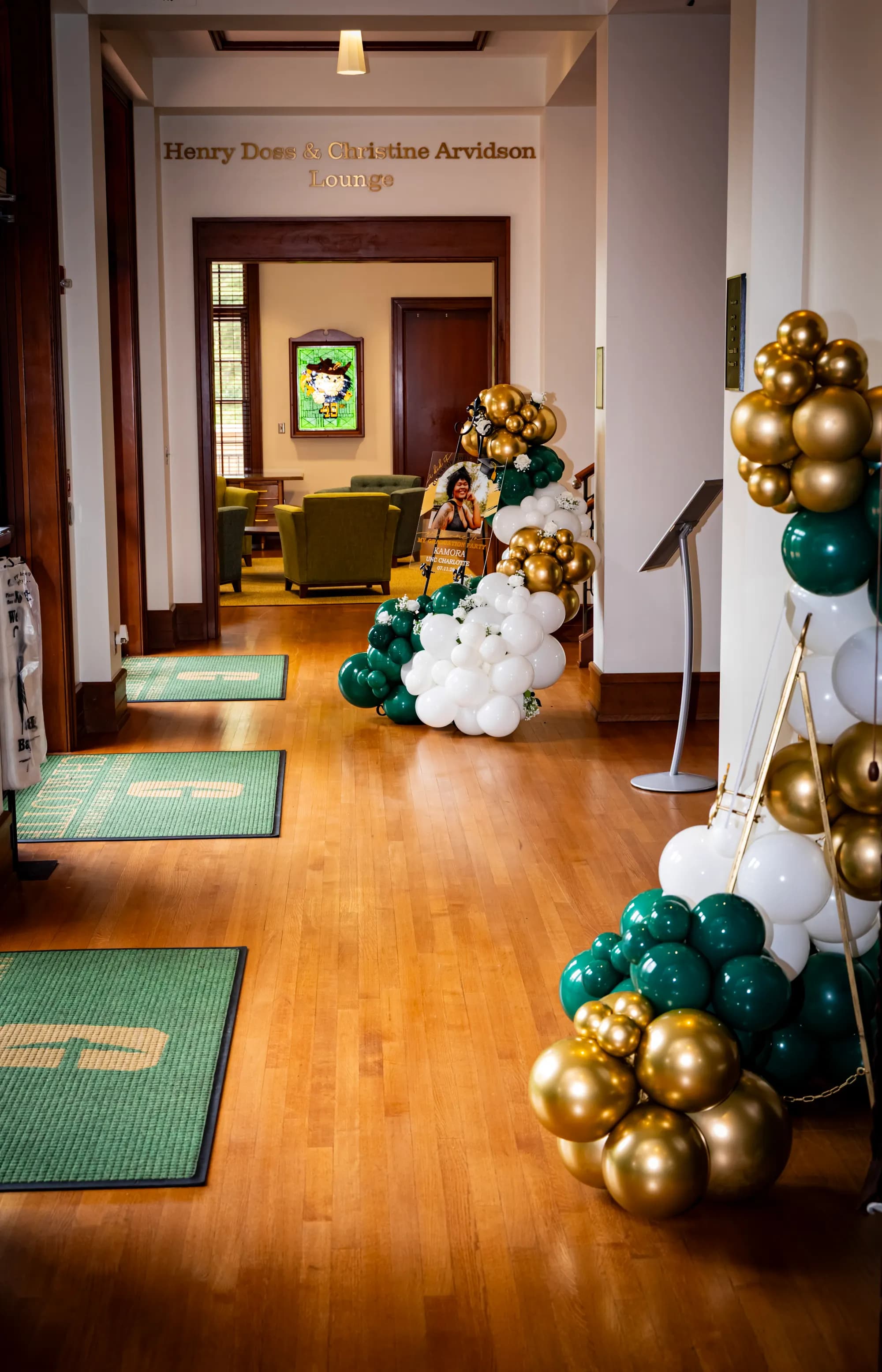 Hallway lined with emerald, white and gold balloon columns leading to a graduation celebration