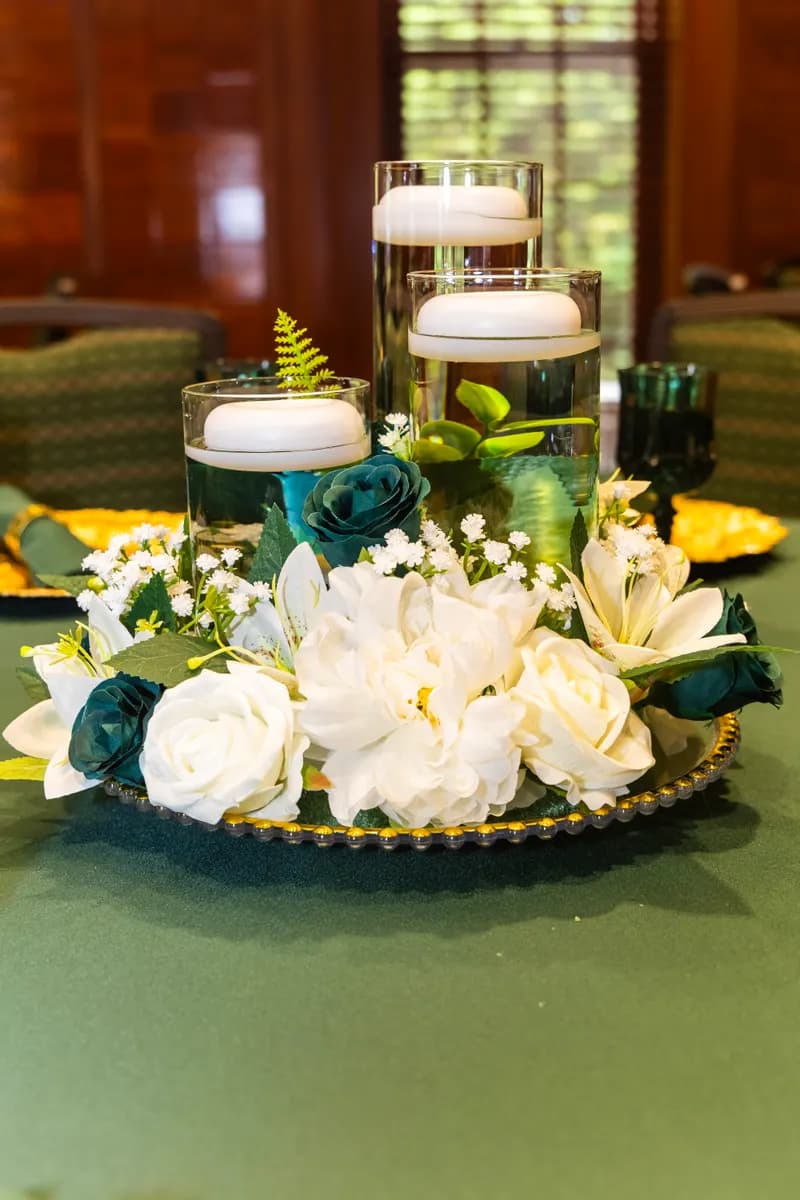 Floating candle cylinders with white roses, lilies and emerald accents