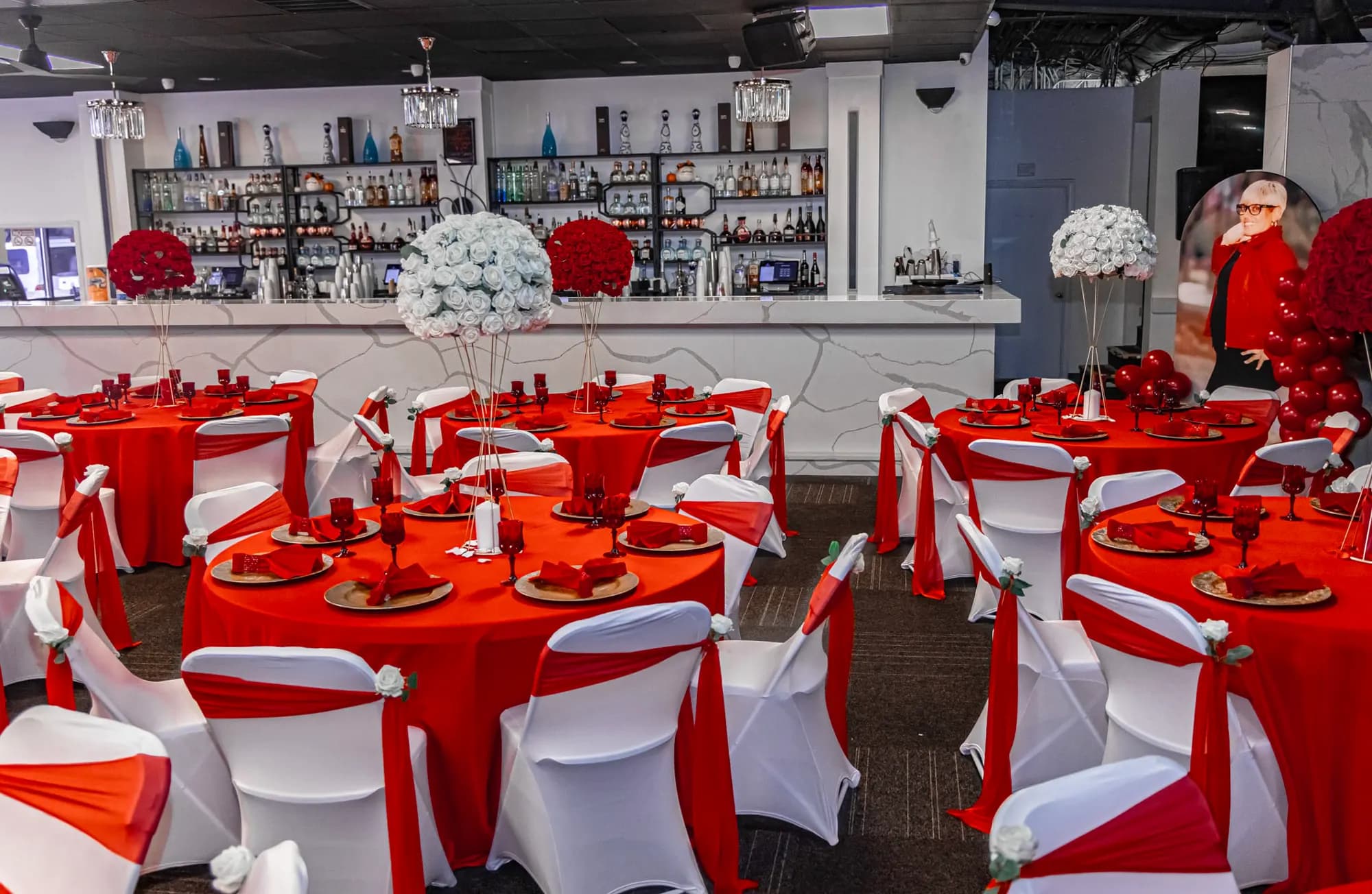 Retirement reception with red linens, white chair covers with red sashes and white and red rose centerpieces