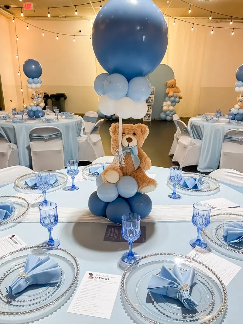Baby shower table with a teddy bear and blue balloon centerpiece and blue glassware